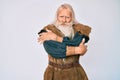 Old senior man with grey hair and long beard wearing viking traditional costume shaking and freezing for winter cold with sad and