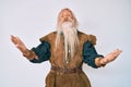 Old senior man with grey hair and long beard wearing viking traditional costume smiling cheerful with open arms as friendly