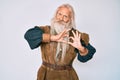 Old senior man with grey hair and long beard wearing viking traditional costume smiling in love doing heart symbol shape with Royalty Free Stock Photo