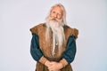 Old senior man with grey hair and long beard wearing viking traditional costume winking looking at the camera with sexy