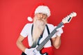 Old senior man wearing santa claus costume playing electric guitar clueless and confused expression Royalty Free Stock Photo