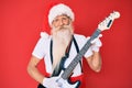 Old senior man wearing santa claus costume playing electric guitar smiling with a happy and cool smile on face Royalty Free Stock Photo