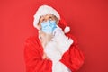 Old senior man wearing santa claus costume wearing safety mask thinking concentrated about doubt with finger on chin and looking Royalty Free Stock Photo