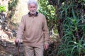 Old senior man in winter sweater outdoors in mountain excursion leaning on walking stick. Caucasian man with beard and white hair Royalty Free Stock Photo