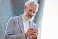 Old senior professional business man holding phone using smartphone outdoor. Royalty Free Stock Photo