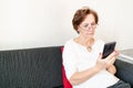 Old senior woman female sit home flat couch hold smartphone write text watch video call alone unhappy sad thinking