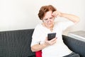 Old senior woman female sit home flat couch hold smartphone write text watch video call alone unhappy sad thinking