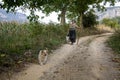 Old senior woman, a peasant, walking with her shepherd dog on a dirtpath in the countryside of Nis, in the Suva planina mountain,