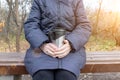 An old senior woman sitting on a bench in late autumn park and holding thermo cup in hands, hot drinks outdoor concept Royalty Free Stock Photo