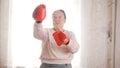 An old senior women boxing in red gloves, looking aggressive and funny