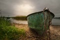 old shabby fishing boat on a chain on the lake with a reed against a dramatic cloudy sky with a glow. picturesque summer landscape Royalty Free Stock Photo