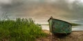 old shabby fishing boat on the lake with a reed against a dramatic cloudy sky with a glow. picturesque summer panoramic landscape Royalty Free Stock Photo