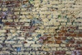 Old shabby red brick wall with spots of yellow, blue and white paint close-up. rough surface texture Royalty Free Stock Photo