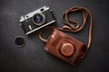 Old shabby retro camera and leather carrying case on black graphite background in close-up, flat lay