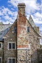 Old shabby vintage stone building with pointed Scandinavian roof and exterior brick chimney