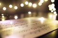 Old sheet with Christmas music notes as background against blurred lights Royalty Free Stock Photo