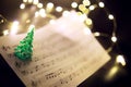Old sheet with Christmas music notes as background against blurred lights Royalty Free Stock Photo