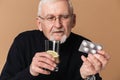 Old sick man with gray hair and beard in eyeglasses and sweater holding glass of pure water with slice of lemon in hand