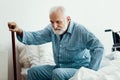 Old sick man with grey beard and hair wearing blue pajamas and sitting on bed at home Royalty Free Stock Photo