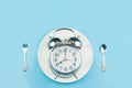 The old silver clock rests on a white plate. With a spoon and fork next to it on blue background,Eating on time concept Royalty Free Stock Photo