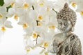 Old silver color statuette Buddha sitting in meditation pose on light blurred orchid flower background