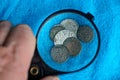 Old silver and copper coins under a magnifying glass on a blue woolen fabric