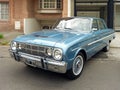 Old sky blue 1960s Falcon four door sedan parked in the street. Classic car show.