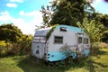 Old small camper trailer with overgrown weeds stuck in the ground.