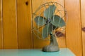 Old small fan on a blue cupboard against a wooden plank wall