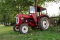 Old small red agriculture tractor parked on the grass summertime before sunset three-quarter view