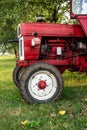 Old small red agriculture tractor parked on the grass summertime before sunset three-quarter view