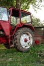 Old small red agriculture tractor parked on the grass summertime before sunset three-quarter view