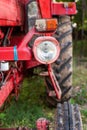 Old small red agriculture tractor parked on the grass summertime before sunset three-quarter view