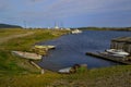 Old small rusty iron boats on green grassy shore of round blue bay, with wood barn on the water. Lake Baikal, village