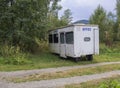 Small white trailer house with blue sign office, abandoned caravan in rural landscape near footpath, green grass and trees Royalty Free Stock Photo