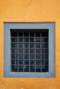 An old small window with a square lattice, like a prison on the yellow wall Royalty Free Stock Photo
