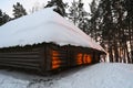 An old snow-covered log house on a hill with a winter sunset on the wall Royalty Free Stock Photo