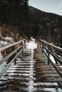 Old snowy bridge in mountains - winter time. Vertical photo of wooden bridge over the wild river with mountains on background Royalty Free Stock Photo