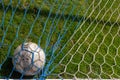 Old soccer ball in the net on the background of grass soccer field. Summer sunny day Royalty Free Stock Photo