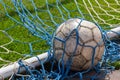 old soccer ball in the net on the background of grass soccer field. Summer sunny day Royalty Free Stock Photo
