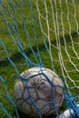 old soccer ball in the net on the background of grass soccer field. Summer sunny day Royalty Free Stock Photo