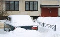 An old Soviet green car covered with snow in the courtyard of a residential building