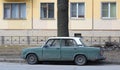 An old Soviet green car with a white roof is parked on the street