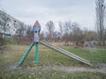 An old Soviet metal slide in the shape of a rocket on a playground against the background of a gloomy autumn landscape.