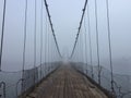 Old spooky suspension bridge foggy entrance. Altai village bridge. Early misty morning