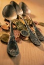 Old spoons and euro and eurocent coins lie on the surface of a wooden table Royalty Free Stock Photo