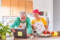 Old spouses enjoy vegetable salad preparation together in kitchen. Caring grey-haired husband feeding loving wife, romantic date, Royalty Free Stock Photo