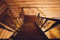 Old squared spiral stairway with dark brown wooden handrails, partly lighted by windows. View from the top.