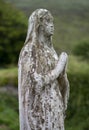 Old statue of Mary or angel in cemetary, covered in moss, praying