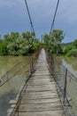 Old steel cable and wooden footbridge across river. Wooden suspension bridge.